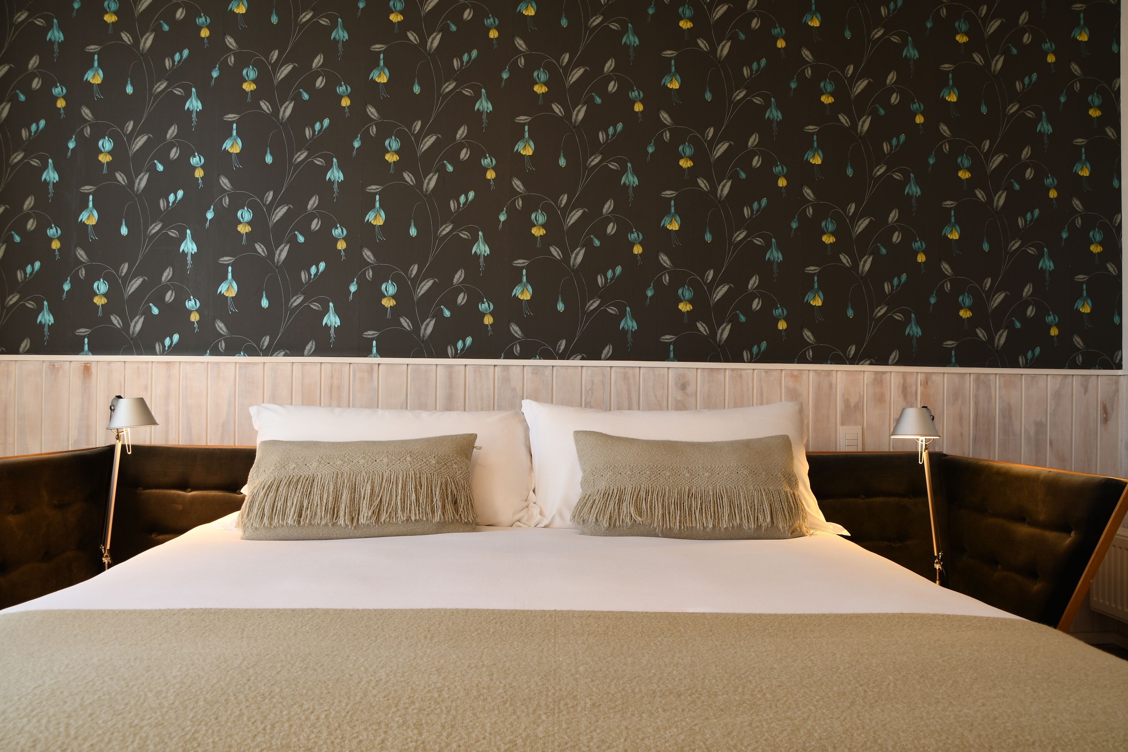 Un lit avec deux oreillers, une tête de lit et un mur orné d’un motif floral.