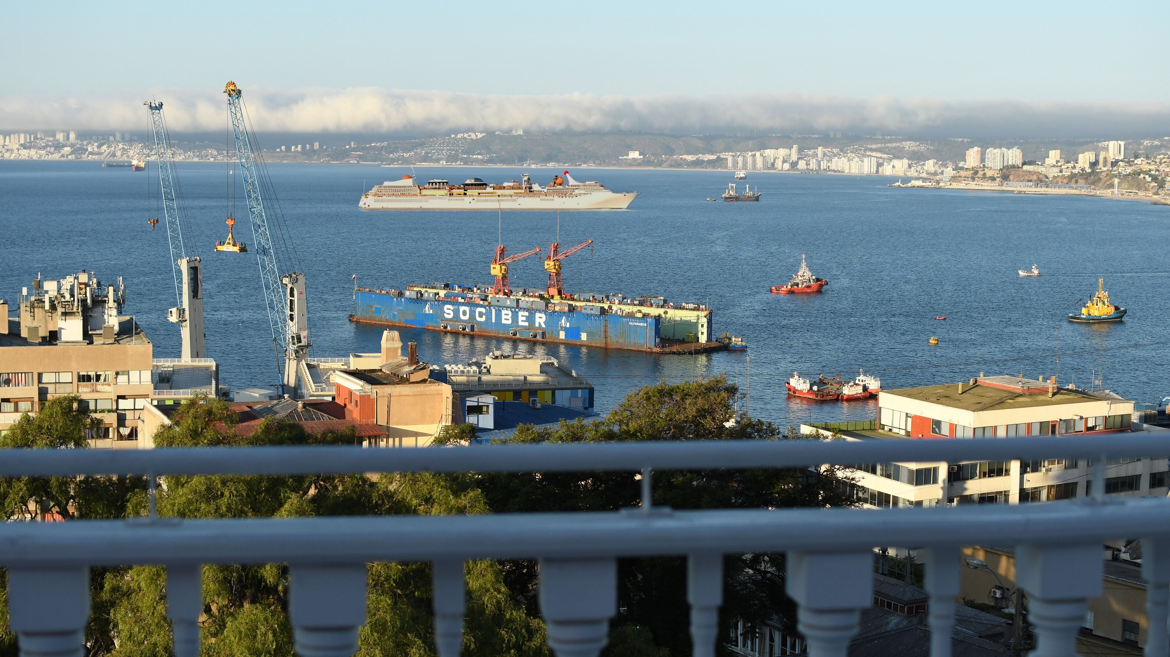 Un port où se trouve un grand navire bleu appelé SOCIBER, des grues et, en arrière-plan, la silhouette d’une ville.
