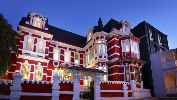 Un edificio grande de estilo victoriano, en rojo y blanco, con múltiples ventanas y una entrada destacada.
