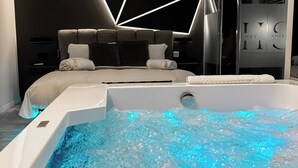 A modern bedroom with a large bed, a separate bathtub, and geometric wall lighting.