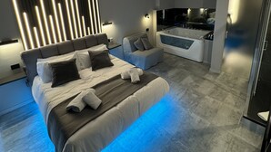 A modern bedroom with a large bed, a seating area, and a kitchenette.