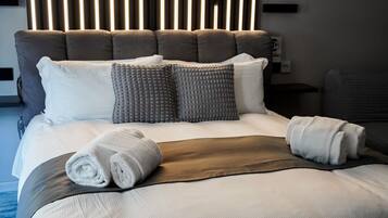 A neatly made bed with a headboard, pillows, and rolled towels.