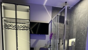 A modern bathroom with a glass shower enclosure, a vanity with a mirror, and a seating area with a chair.