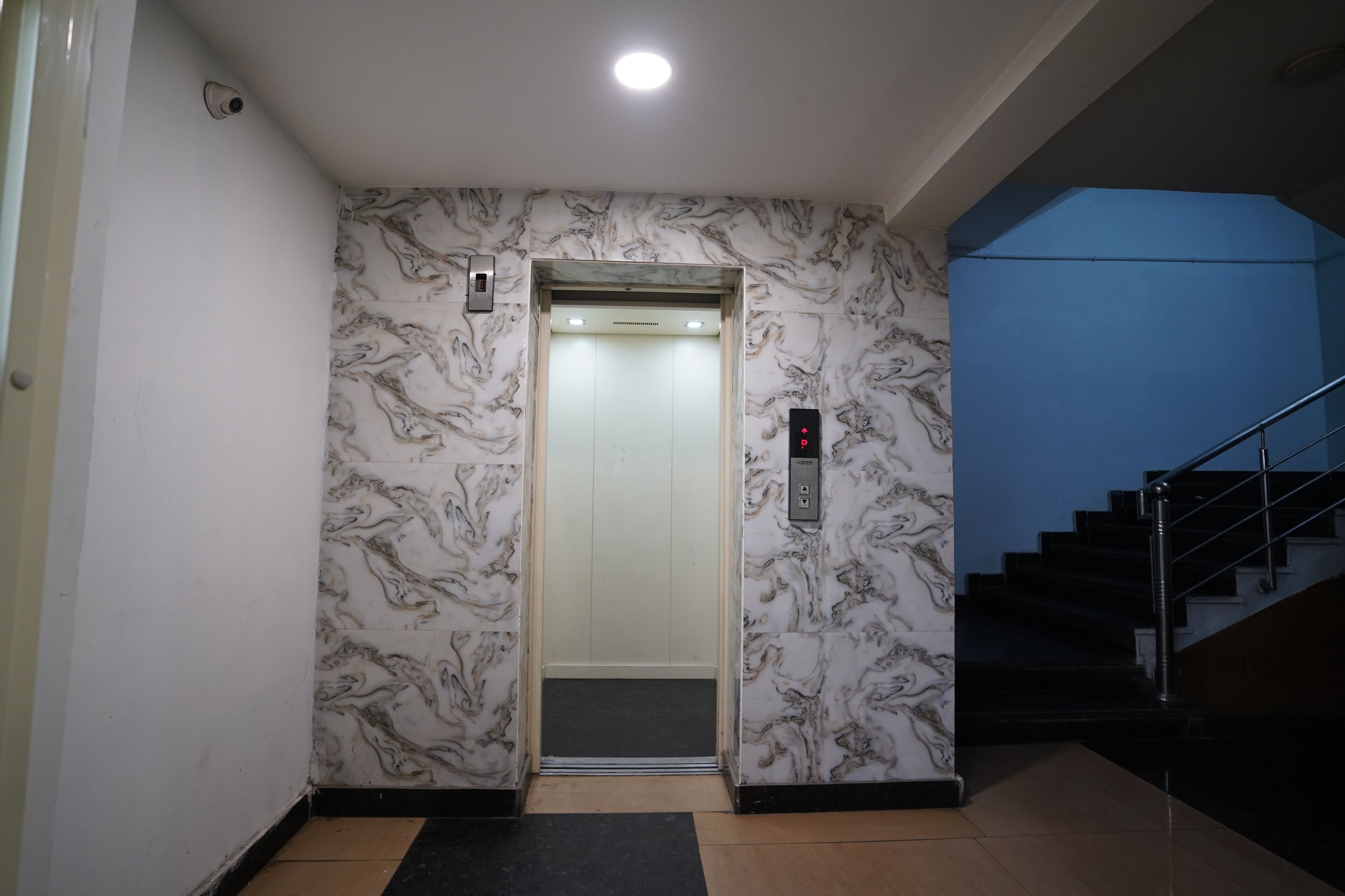 An elevator with marble-patterned walls, a black mat at the entrance, and a blue wall to the right.