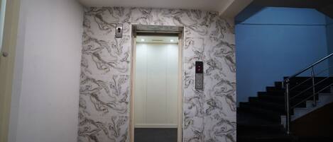 An elevator with marble-patterned walls, a black mat at the entrance, and a blue wall to the right.
