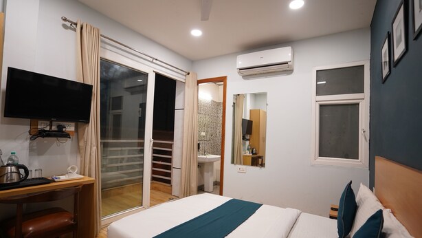 A hotel room with a bed, a desk, a television, a window, and an air conditioning unit. - Hotel Lyf Corporate Suites - Peera Garhi (New Delhi)