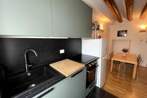 A modern kitchen with a black countertop, a wooden cutting board, a white refrigerator, and a dining table with chairs.