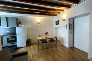 A compact kitchen with a dining area, wooden beams on the ceiling, and a white door.
