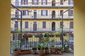 Un balcón con plantas en macetas y vista a un edificio amarillo con varios balcones.