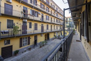 A multi-story yellow building with balconies, potted plants, and a narrow street.
