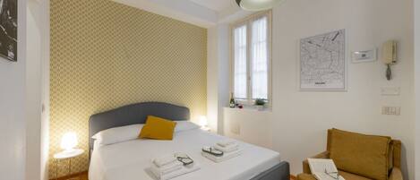 Habitación de hotel con cama, una silla, un mapa en la pared y una ventana.