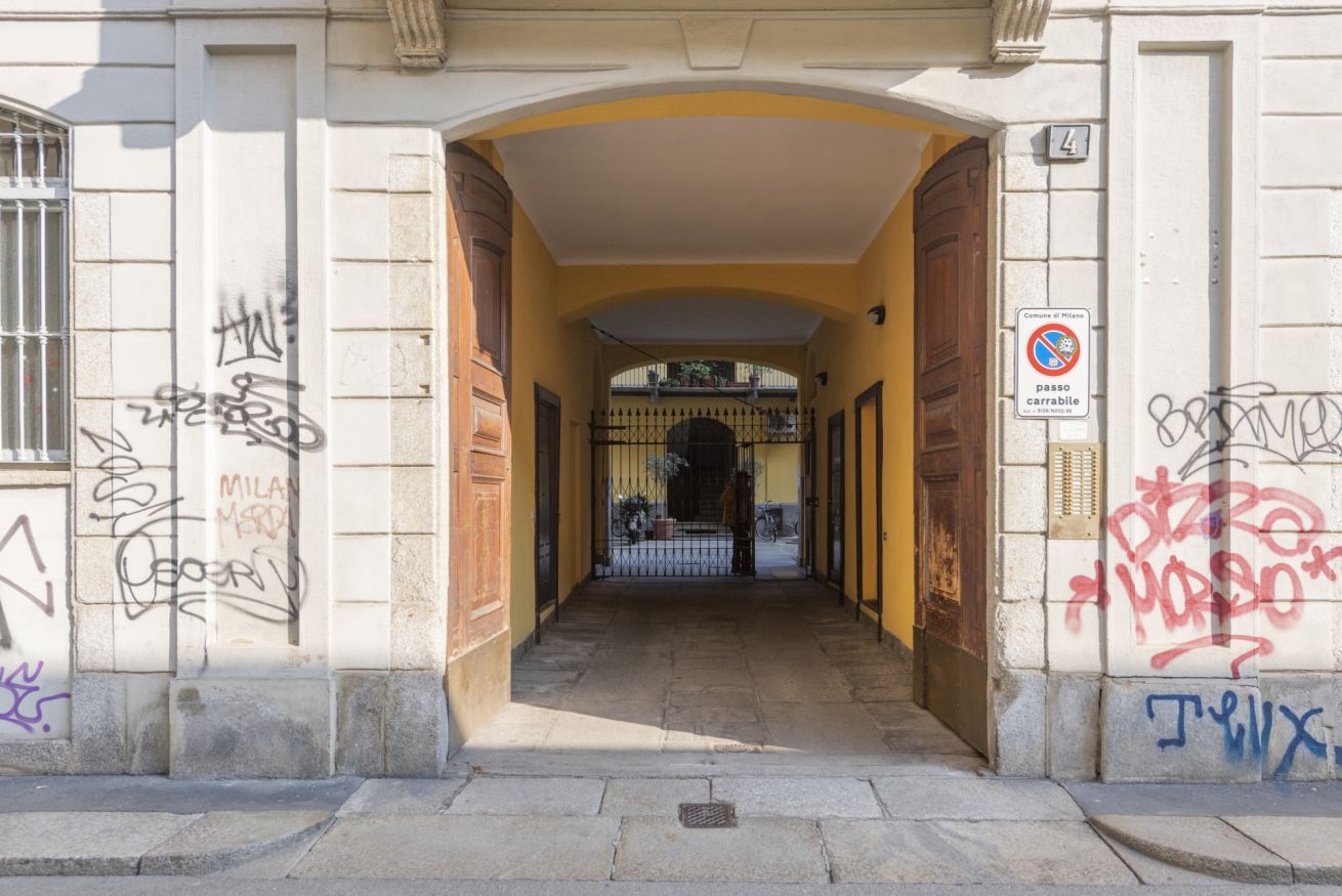 Entrada de un edificio con patio amurallado, grafitis en las paredes y un cartel de prohibido estacionar.