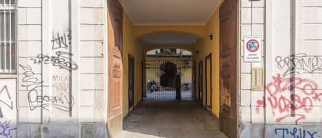 Entrada de un edificio con patio amurallado, grafitis en las paredes y un cartel de prohibido estacionar.