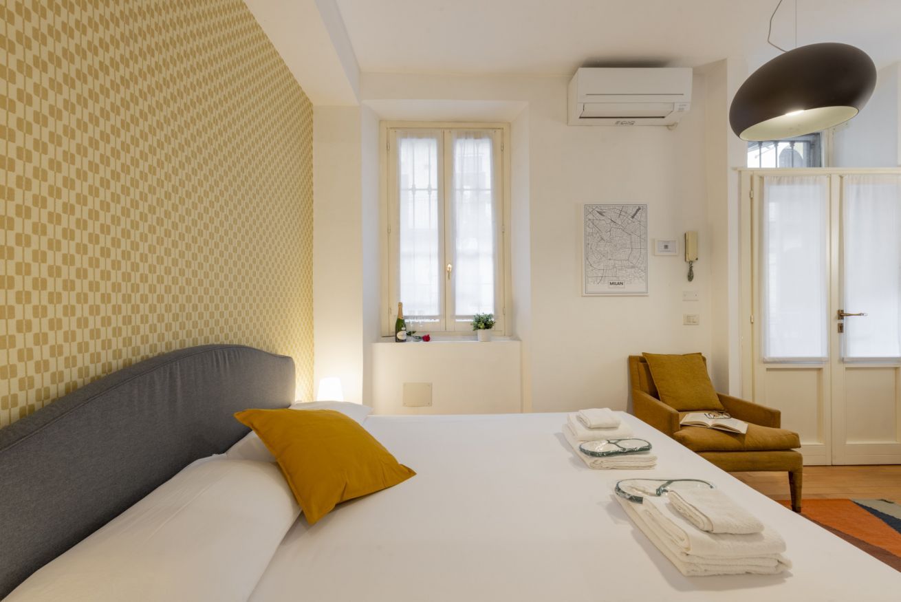 Habitación de hotel con una cama, una ventana, una silla y aire acondicionado de pared.
