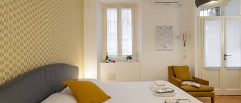 Habitación de hotel con una cama, una ventana, una silla y aire acondicionado de pared.