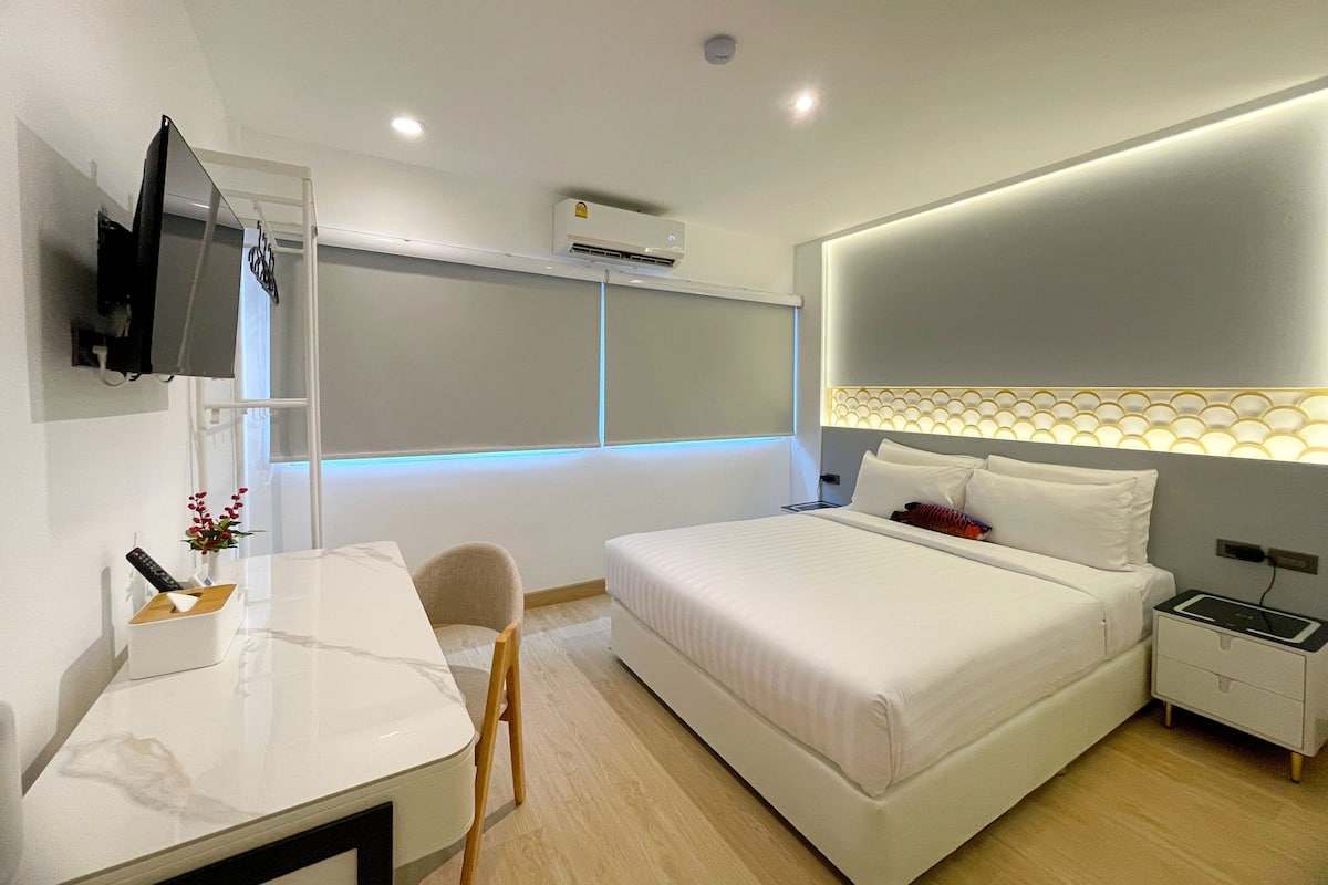 Une chambre d’hôtel moderne équipée d’un lit, d’une table de chevet, d’une chaise, d’un bureau, d’une télévision et d’un climatiseur fixé au mur.