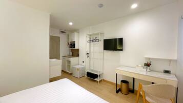 A modern hotel room with a bed, a desk, a TV, and a shower area.