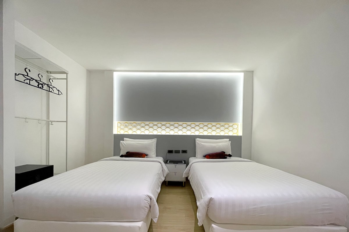 Une chambre d’hôtel avec deux lits simples, un grand miroir, une table de chevet et un téléviseur fixé au mur.