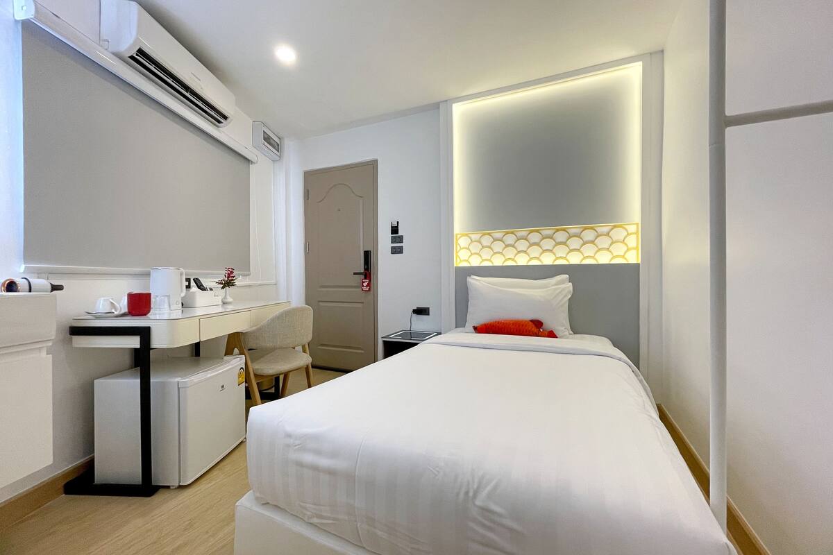 Une chambre d’hôtel équipée d’un lit, d’un bureau, d’une chaise, d’un appareil de climatisation et d’une table de chevet.