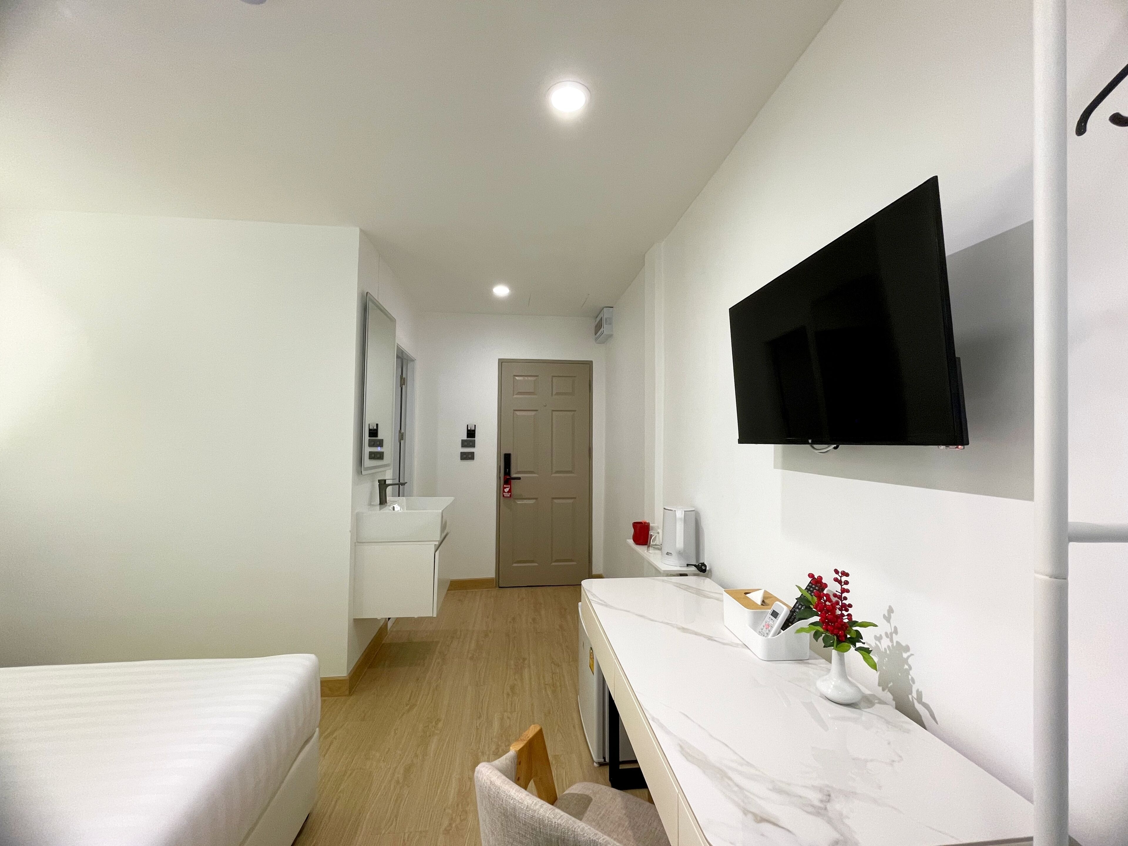 A hotel room with a bed, a desk with a TV, a mirror, a sink, and a door.
