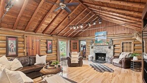 L’intérieur d’une cabane en rondins, avec une cheminée, des canapés en cuir et un ventilateur de plafond.