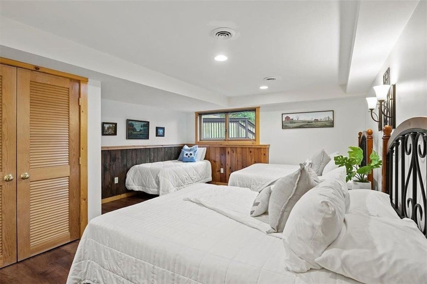 A bedroom with two beds, wooden paneling, a window with a view, and a door.