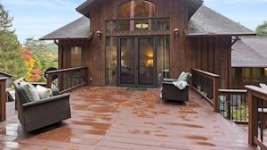 Une cabane en bois dotée d’une terrasse, de deux fauteuils en osier et d’une porte d’entrée en verre.