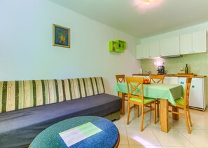 Une petite pièce agréable et chaleureuse, avec un canapé, une table à manger et des chaises, un petit coin cuisine et une petite table ronde avec un coussin.