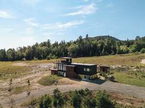 Una moderna casa a due piani con un'ampia terrazza e un garage, immersa in un pendio boscoso.