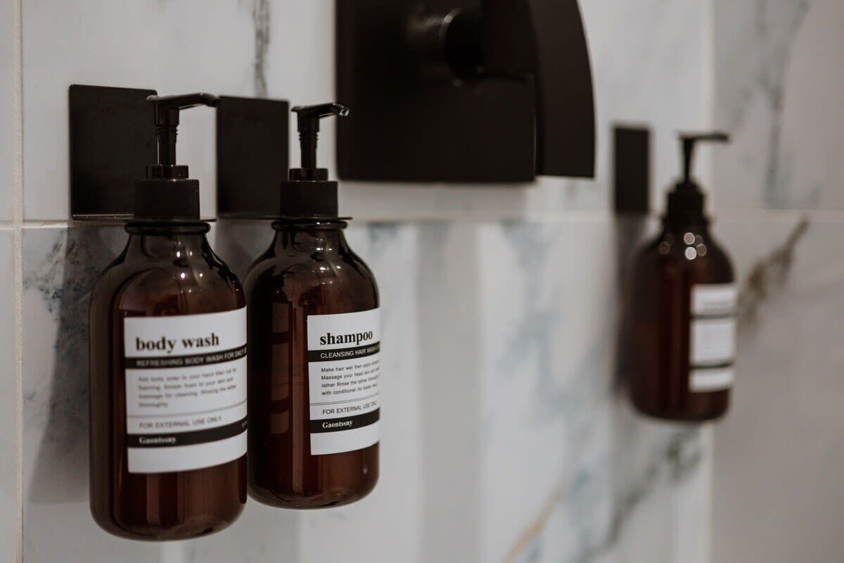 Zwei Flaschen Duschgel und Shampoo hängen an einer gefliesten Wand.