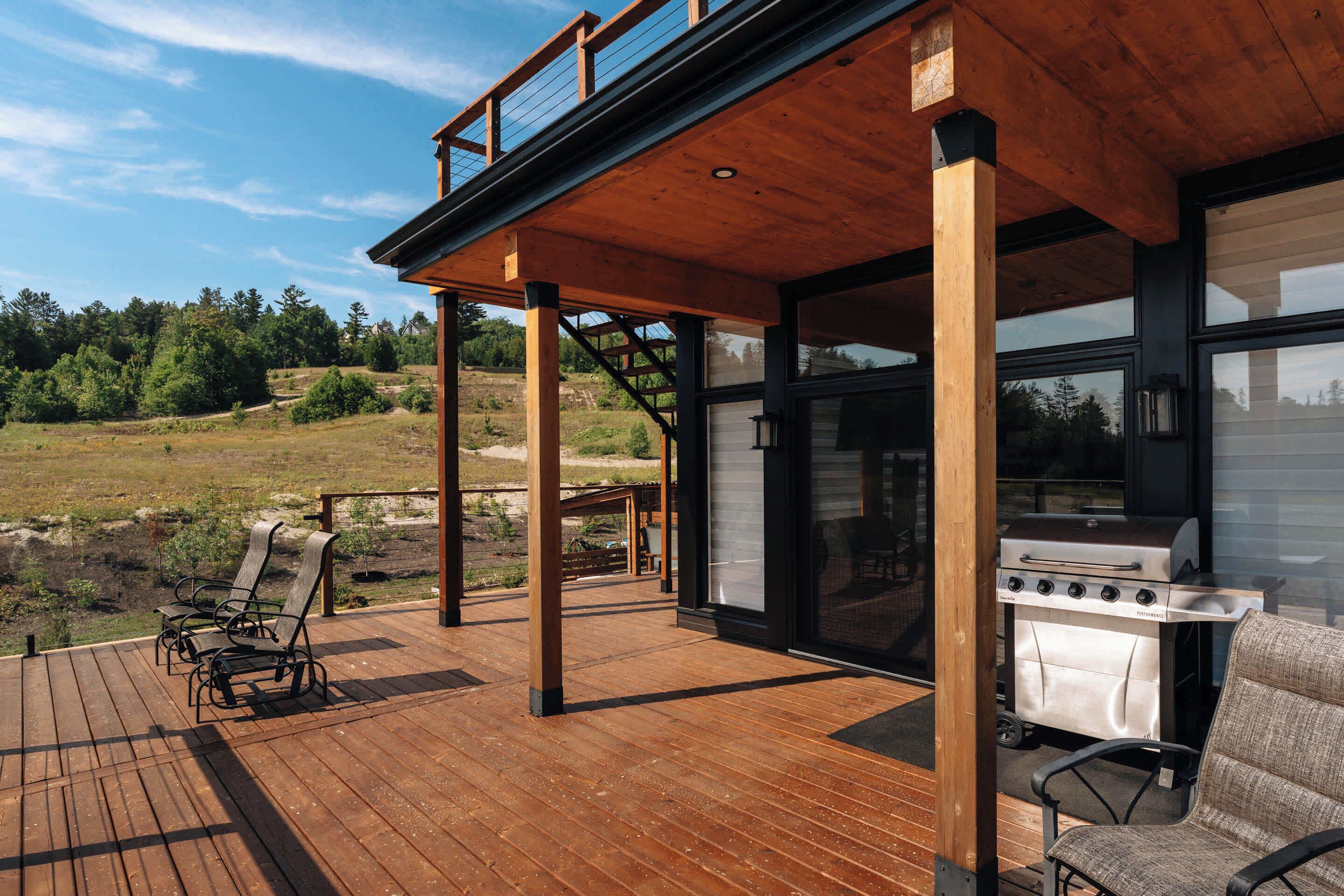 A wooden deck with outdoor seating, a grill, and a view of a natural landscape.