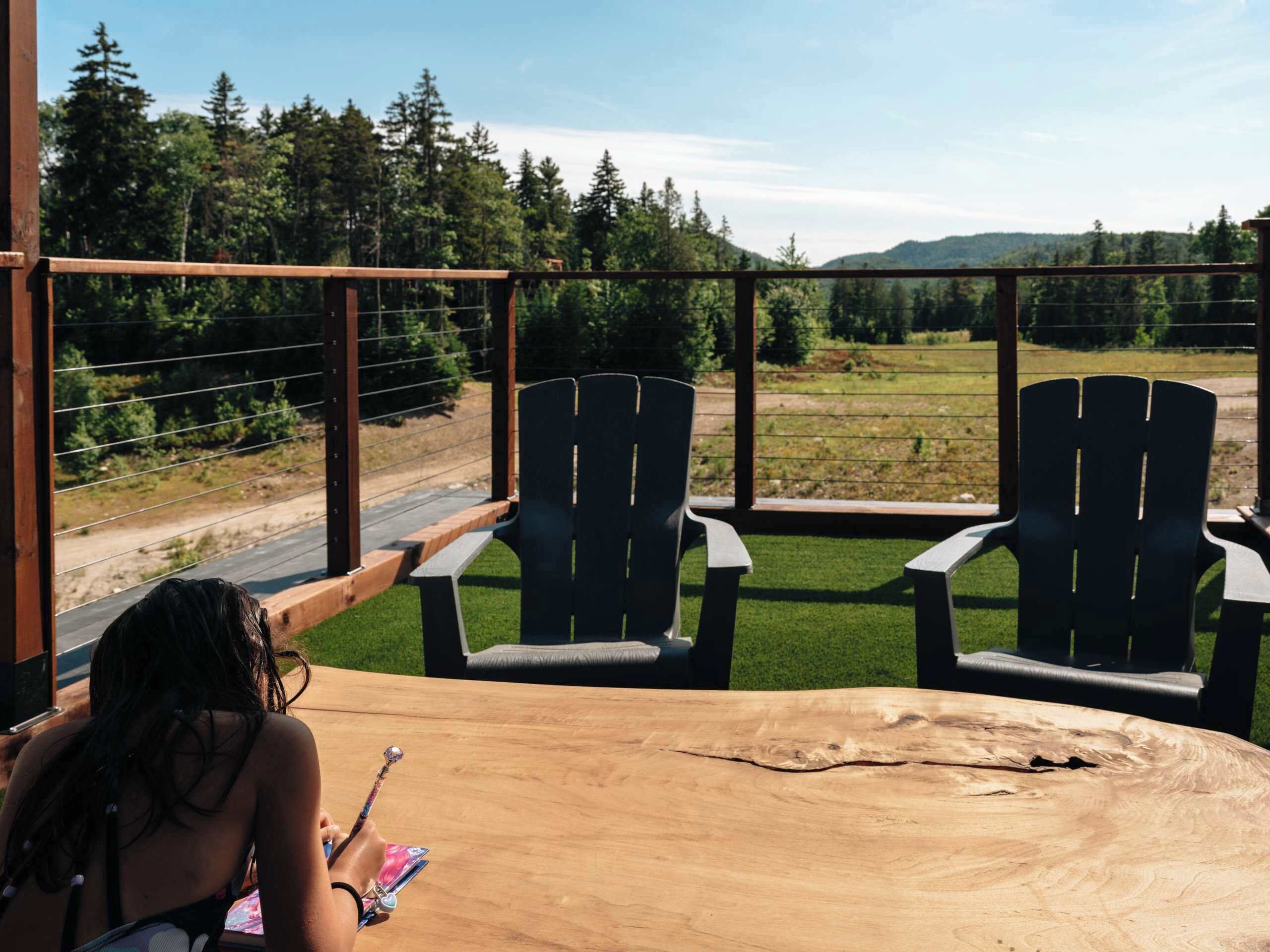 A wooden table with two Adirondack chairs facing a scenic view of a forest and mountains.