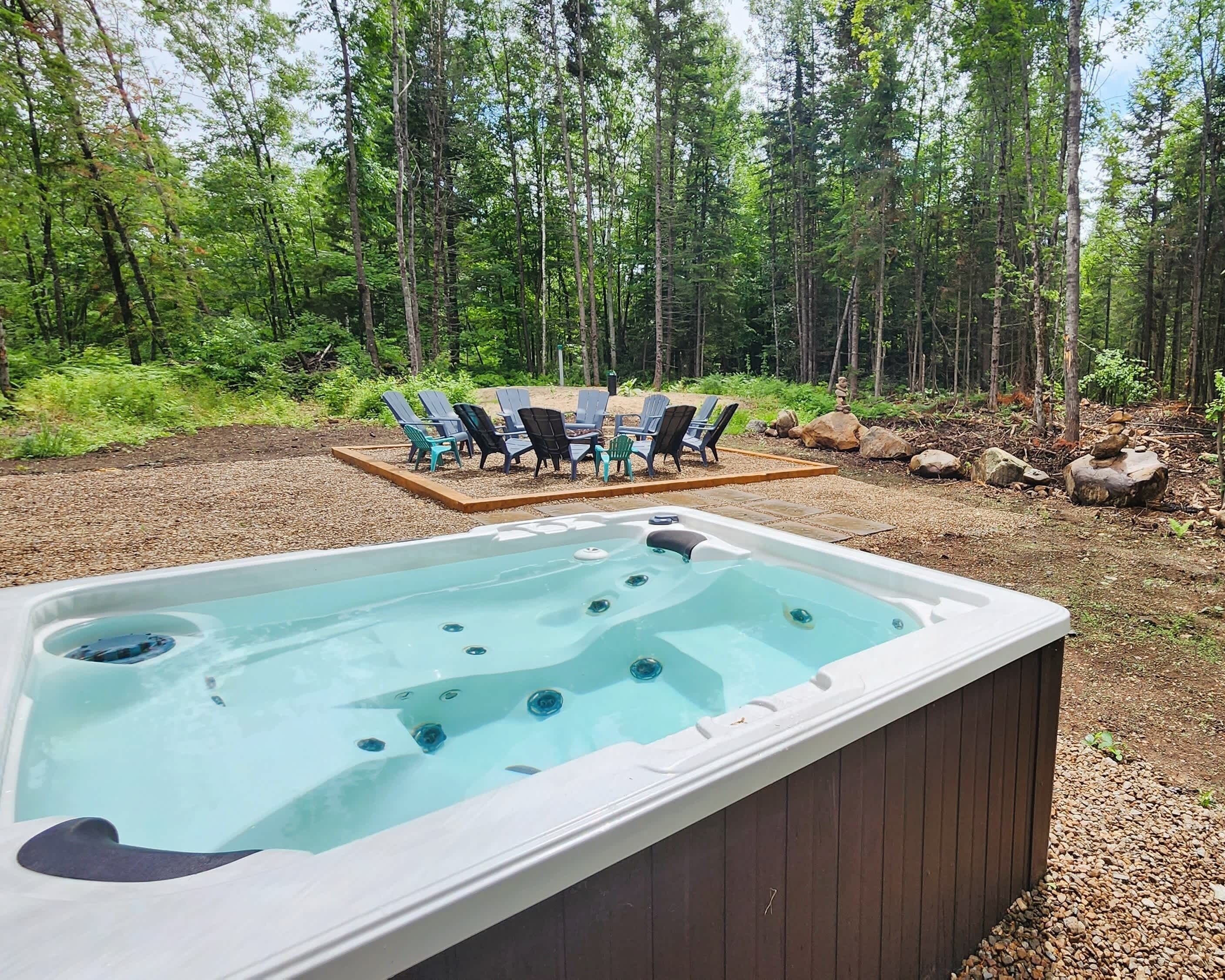 Un jacuzzi con chorros, rodeado de asientos exteriores y un bosque al fondo.