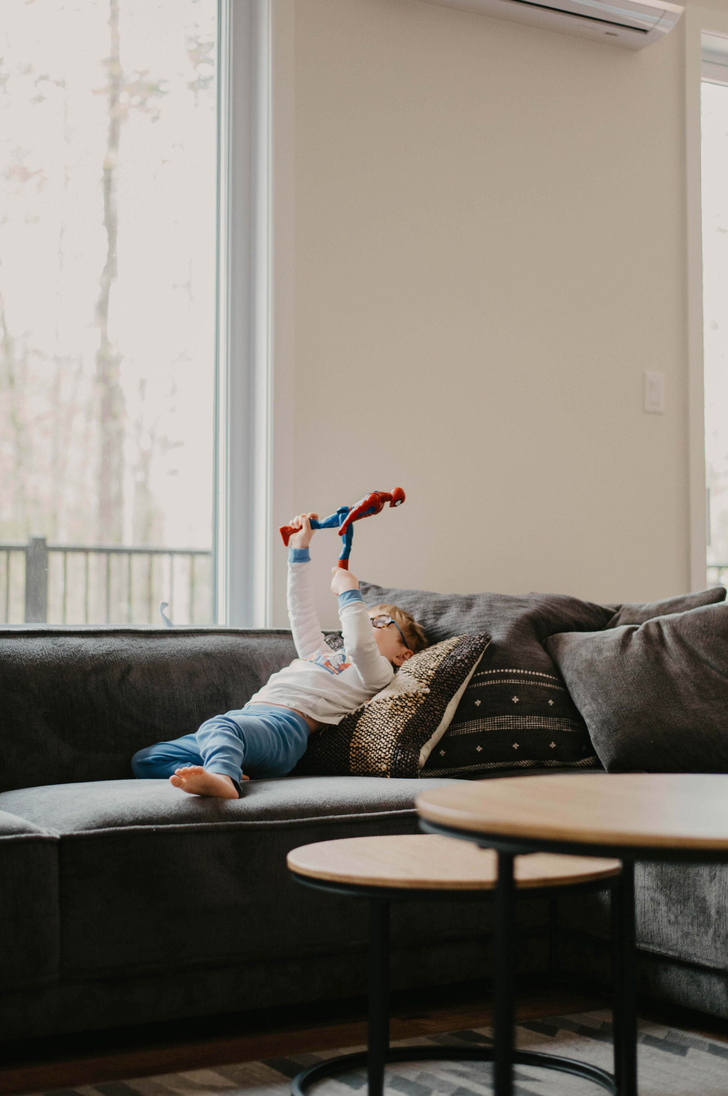 A child lying on a dark grey sofa with a window behind them.