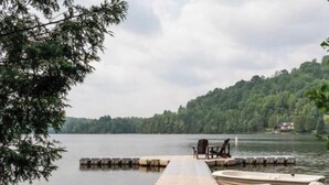 A dock with a rowboat and a chair by the water, surrounded by trees and a house in the background. - Peaceful Chalet Tremblant, hot tub lakes & Kayaks (Amherst)
