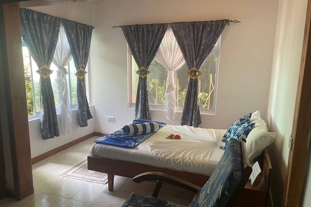 Un dormitorio con una cama, una silla y dos ventanas con cortinas.