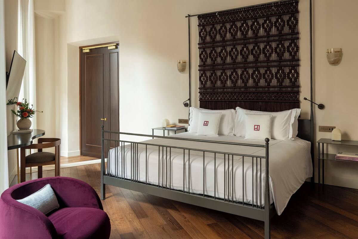 A modern bedroom with a metal bed frame, a decorative headboard, a bedside table with a lamp, and a chair.