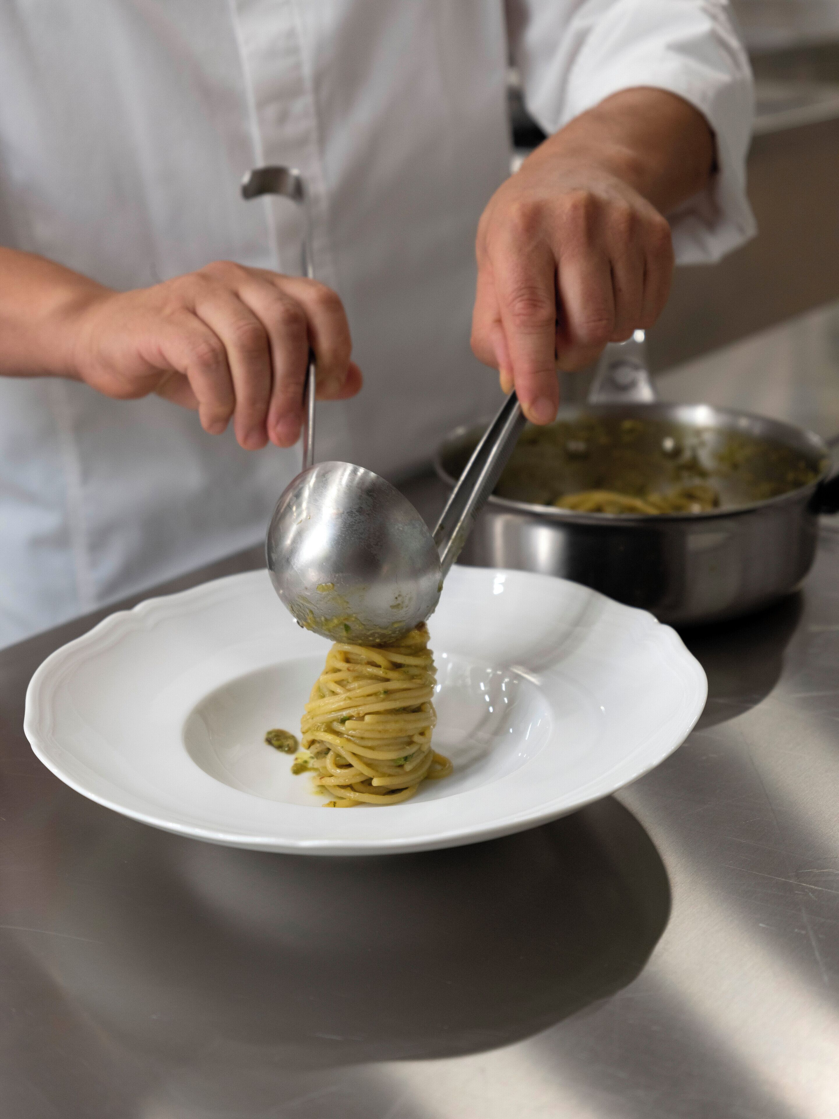 Una persona che serve spaghetti su un piatto bianco.