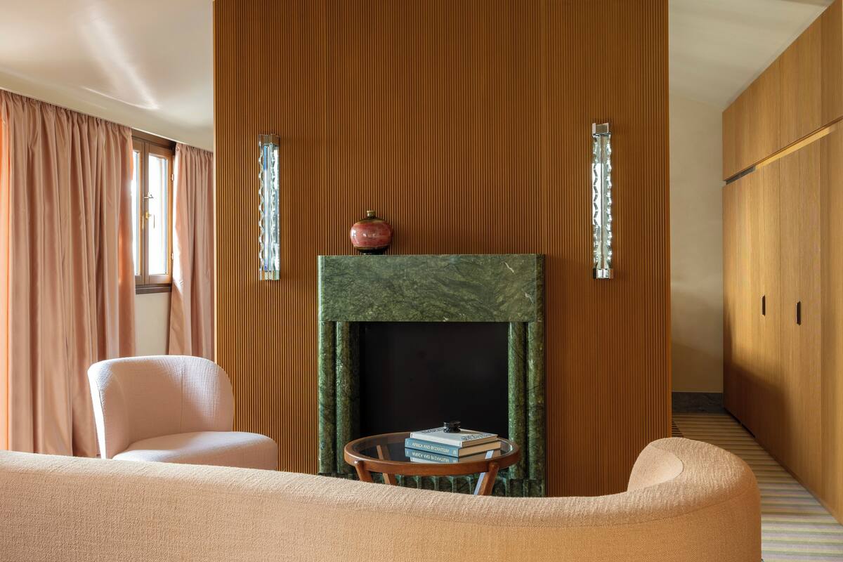 A room with a fireplace, two armchairs, a small table, and a wooden panel wall.