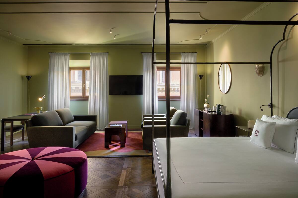 A hotel room with a bed, two sofas, a small table, a desk, a chair, and a TV.