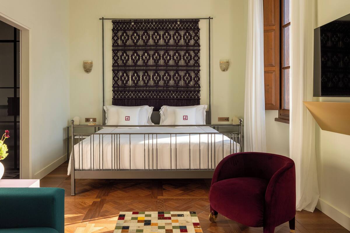 A neatly arranged bedroom with a bed, a chair, and a patterned headboard.