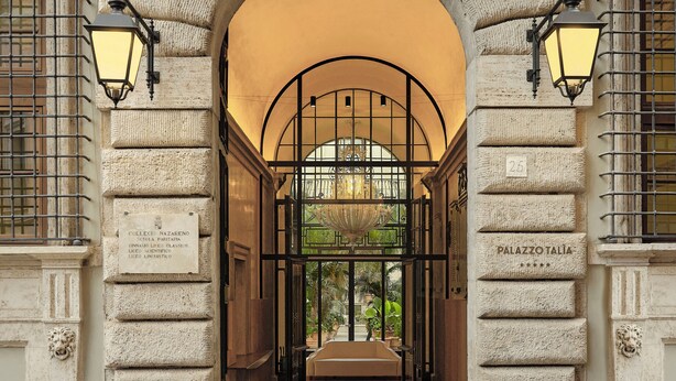 An entrance with a stone archway, two wall-mounted lamps, and a sign reading "Palazzo Talia." - Palazzo Talìa - Small Luxury Hotels of the World (Rome)