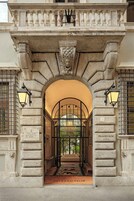 Una entrada con un arco de piedra, dos lámparas de pared y un cartel que dice "Palazzo Talia".