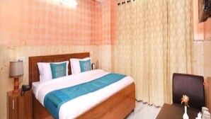 A bedroom with a wooden bed, a nightstand, a desk with a vase, and a curtain. - Hotel Mount View Shimla (Shimla)