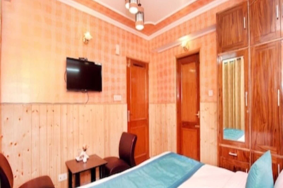 Un dormitorio con cama, televisor montado en la pared, escritorio y silla.