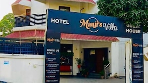 En hotelindgang med et skilt for 'Mauji's Villa' og 'Guest House'. Der er bannere, der reklamerer for booking til forskellige arrangementer.