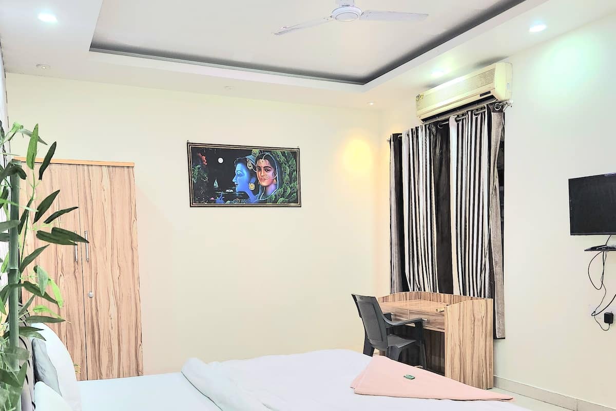 Een moderne slaapkamer met een bed, bureau en stoel, een plafondventilator en een aan de muur bevestigde televisie.