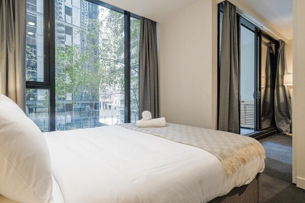 Une chambre d’hôtel avec un grand lit, une fenêtre avec des rideaux et une vue sur les bâtiments et les arbres à l’extérieur.