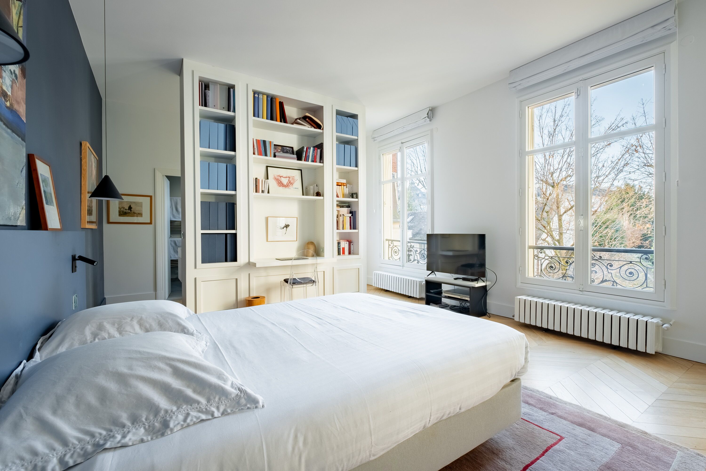 Een slaapkamer met een groot bed, inbouwboekenplanken, een televisie en uitzicht op de omgeving door grote ramen.