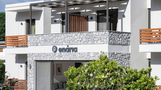 A modern building with a stone facade, a balcony with wooden slats, and a sign that reads "enana".